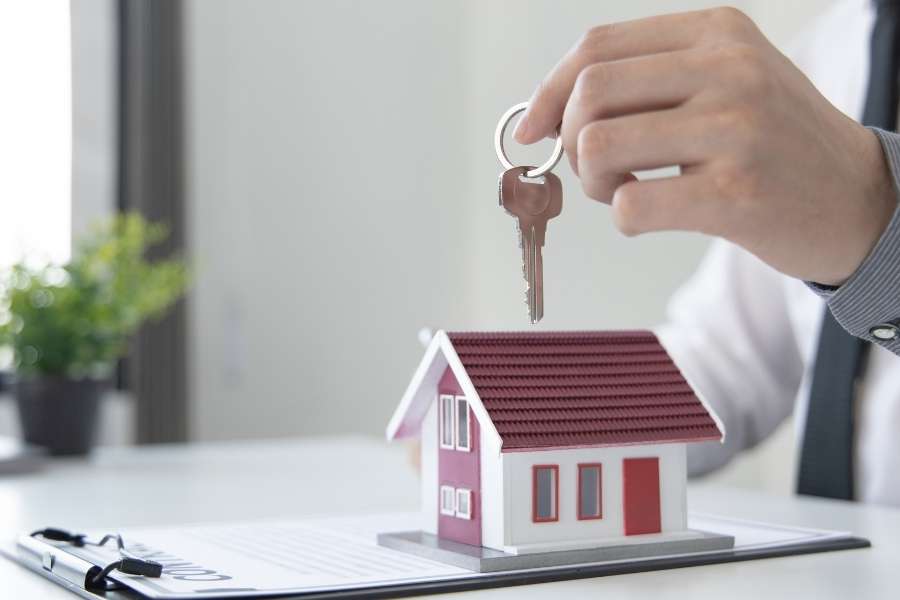 Une main tenant des clés au-dessus d'une maquette de maison, symbolisant la gestion immobilière via une SCI.
