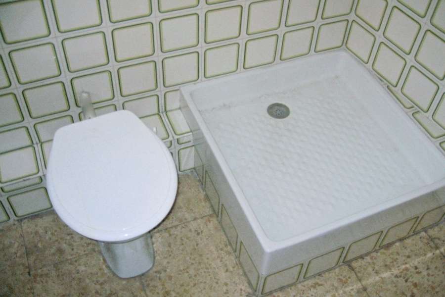 Vue en plongée d'une petite salle de bain ancienne avec un WC blanc et un receveur de douche carré installés côte à côte sur un carrelage à motifs.