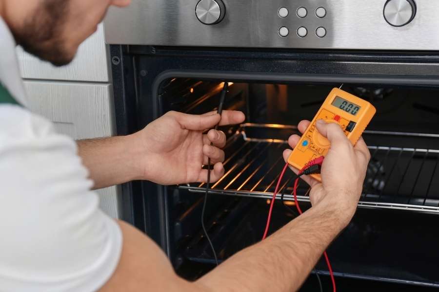 Un technicien teste les composants électriques d'un four encastrable à l'aide d'un multimètre numérique orange.