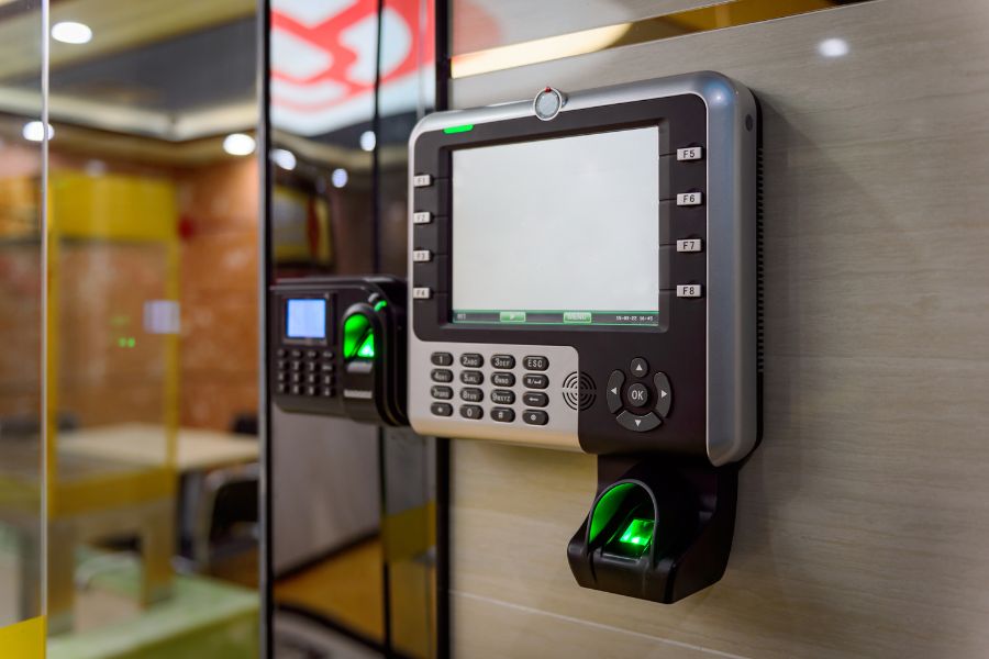 Un terminal électronique moderne doté d'un écran, de touches et d'un lecteur d'empreintes digitales lumineux, illustrant un système de contrôle d'accès par badge ou biométrie à la maison.