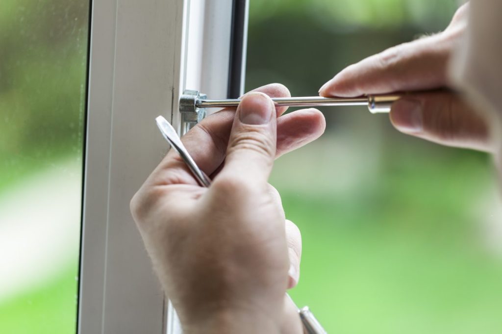 Un gros plan montre les mains d'une personne qui utilise un outil pour regler gond et paumelle menuiserie pvc sur un profilé de fenêtre