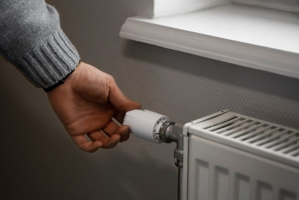 Main réglant un robinet thermostatique blanc sur un radiateur mural pour un diagnostic panne facile chauffage.